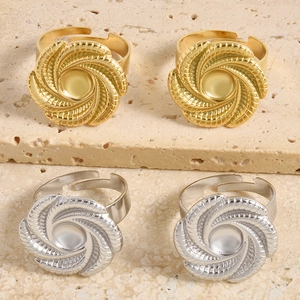 Detailansicht von Spirale-Blumenringen in Gold und Silber auf einer beigen Sandsteinplatte