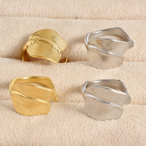 Detailed macro view of gold and silver feather-shaped adjustable rings on beige velvet