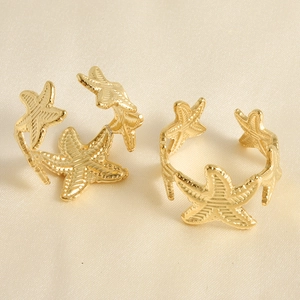 Detailed close-up of two golden starfish open rings on white silk texture fabric