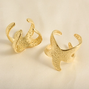 Close-up of golden starfish rings with textured surface on white silk fabric background