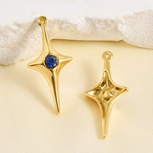 Detail of gold four-pointed star pendants with deep blue gemstone on neutral stone surface