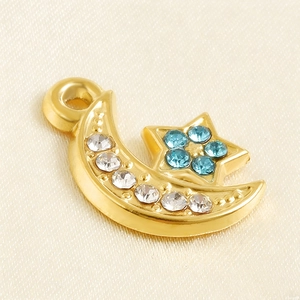 Détail du pendentif lune et étoile doré avec strass blancs et bleus sur fond de soie