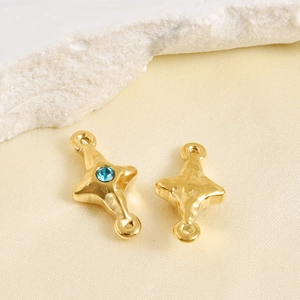 Close-up of golden four-pointed star jewelry connectors with blue stone and hammered texture