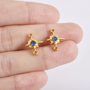 Detail of gold starburst pendants with blue stones held in hand for necklace DIY