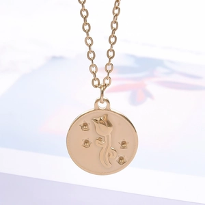 Vue détaillée du pendentif rond en acier doré avec motifs tulipe et étoiles en relief