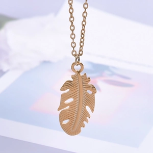 Gros plan détaillé d'un pendentif feuille de monstera dorée sur une chaîne délicate