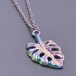Gros plan sur un pendentif feuille de monstera en acier inoxydable aux reflets arc-en-ciel