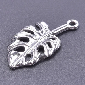 Détail macro d'un pendentif feuille de monstera en acier argenté avec texture ajourée