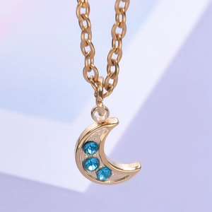 Macro shot of gold crescent moon pendant with three blue rhinestones on O-chain necklace