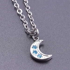 Macro view of silver crescent moon pendant with three blue rhinestones and cross chain