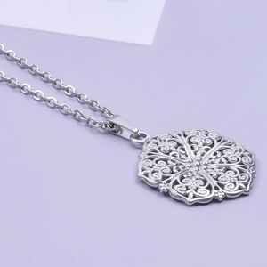 Macro-opname van een zilveren roestvrijstalen hanger met holle bloemen gravure en ketting