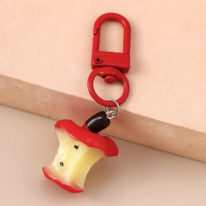 Detailed view of apple core keychain with red snap hook on beige stone surface