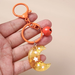 Creative moon resin keychain with star sequins and red bell, held in hand for scale