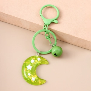 Close-up of green resin moon keychain with gold foil flakes and small bell charm