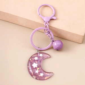 Detail of purple resin moon keychain with stars, metal bell and clasp on beige background