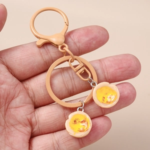 Detailed view of handmade fried egg resin charms on a yellow metallic keyring held in hand