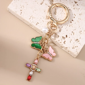 Nahaufnahme von goldenem Schmetterlings-Schlüsselanhänger mit Kristallkreuz auf Stein