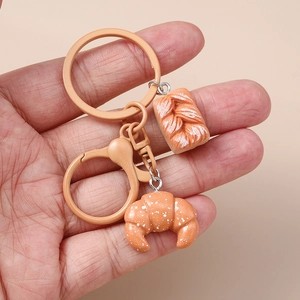 Detailed view of handmade resin baguette and croissant keychain held in hand