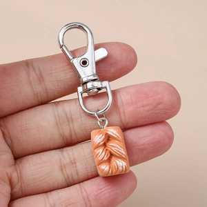 Close-up of creative baguette bread keychain held by hand with silver metal clasp detail