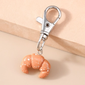 Macro detail of a realistic croissant keychain charm with textured resin finish and silver clasp