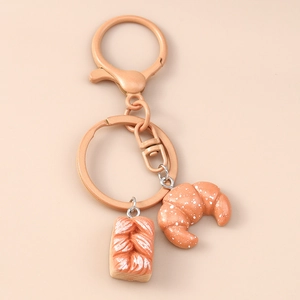Detailed macro view of realistic 3D croissant and bread pendants on a matte keychain