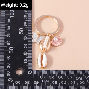 Detail of gold keychain with butterfly, pearl shell, and enamel sea charms on pink background