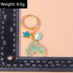 Detail of mermaid tail keychain with blue starfish and shell on minimalist gold ring