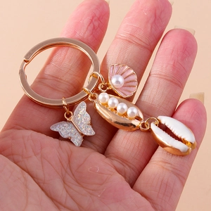 Golden mermaid tail keychain featuring butterfly shells and pearls held in hand
