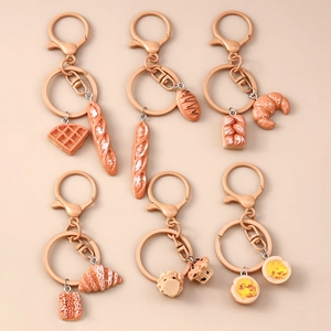 Flat lay macro of realistic croissant, baguette, and tart pendant keychains on beige surface