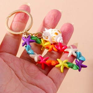 Colorful starfish and conch keychain with gold metal ring held in hand