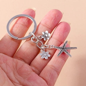 Detail of vintage silver starfish and flower charms on a metal keychain held in hand
