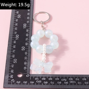Macro detail of a light blue beaded bow keychain with pearls and flower charm on pink background