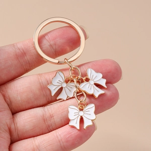 Detail of three white enamel bow pendants with golden zinc alloy rings on a keychain