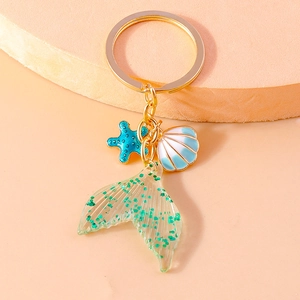 Detail of mermaid tail keychain with blue starfish and shell on a warm orange backdrop