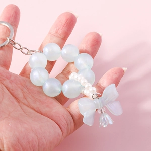 Handheld light blue beaded keychain with pearl bow and bell pendant on pink background