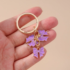 Chic golden keychain featuring three elegant purple enamel bow pendants for handbag decor
