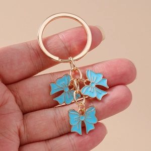Golden keychain featuring three sky blue enamel bow pendants held by a hand