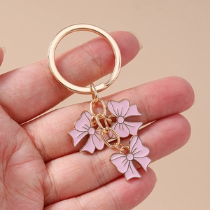 Handheld view showing three pink enamel bow charms on a gold-plated keychain ring