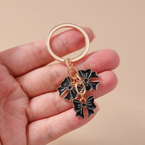 Close-up of golden keychain with three black enamel bow charms and polka dot details