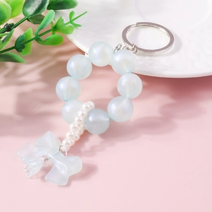 Detail of beaded keychain with blue bow pendant and faux pearls on a pastel background