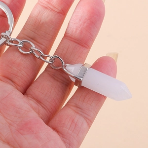 Close-up of a white hexagonal crystal bullet keychain being held on a pink background