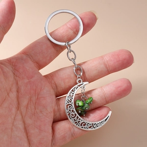Detail of silver alloy crescent moon keychain with green turquoise stones held in hand
