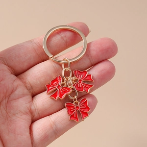 Handheld view of a trendy gold keyring featuring three red enamel bow pendants