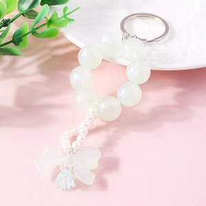 Detail of beaded keychain with pearl-like beads, white bow, and blue flower pendant