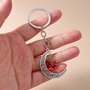 Detailed close-up of a vintage crescent moon keychain with red beads held in hand