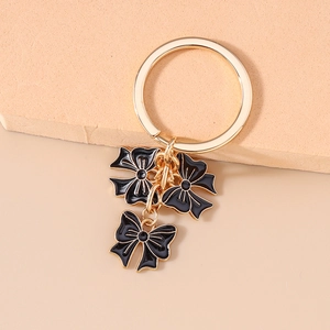 Detail showing gold metal bow keychain with black enamel drips and polished finish