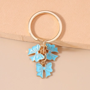 Detail of a golden keychain ring with three light blue enamel bow pendants on a pink surface