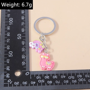 Pink alpaca keychain with rainbow charm measured on a ruler for size reference