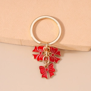 Detail of golden keychain with three red enamel bow pendants on a minimalist background