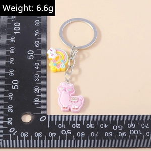 Detail view showing a cute pink alpaca and rainbow cloud keychain next to a ruler for scale